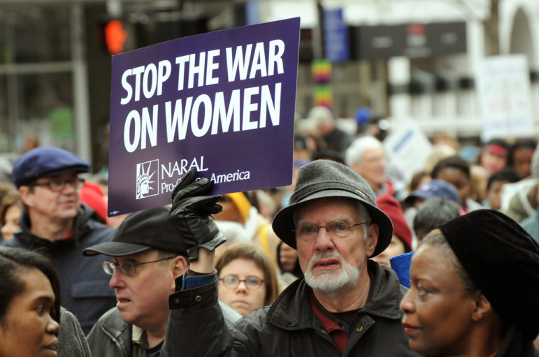Mac Hulslander, of Raleigh, carries a "Stop the War on Women" sign as an estimated 15 to 20,000 people march down Fayetteville Street.