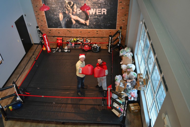 Adam Grossman poses in the ring with Ryan McGee at the Title Boxing Club in Cary. Behind them and against the window are thousands of donated socks.