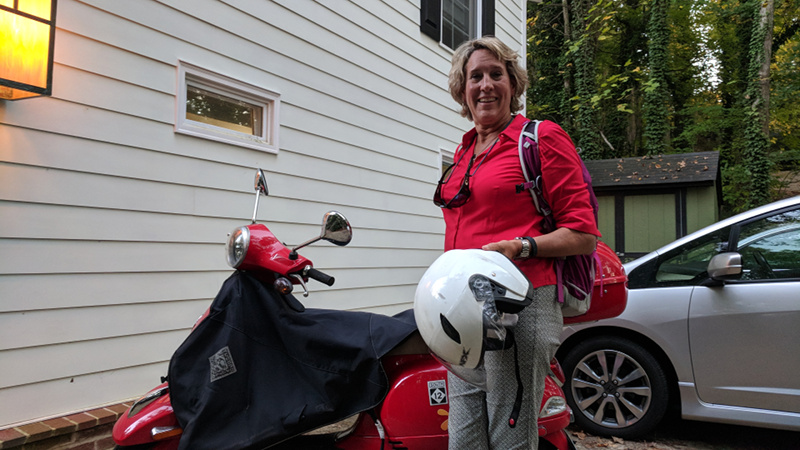Gretchen stands in front of her red Vespa.